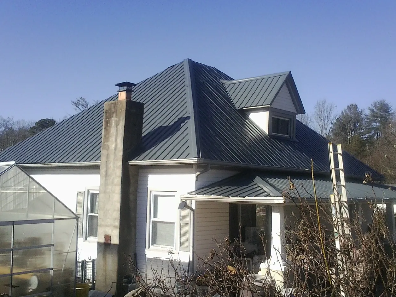 Dark blue standing seam metal roof on a white farmhouse with dormer — Slate & Tile Roof Repair by Roofing Brothers in Shoup