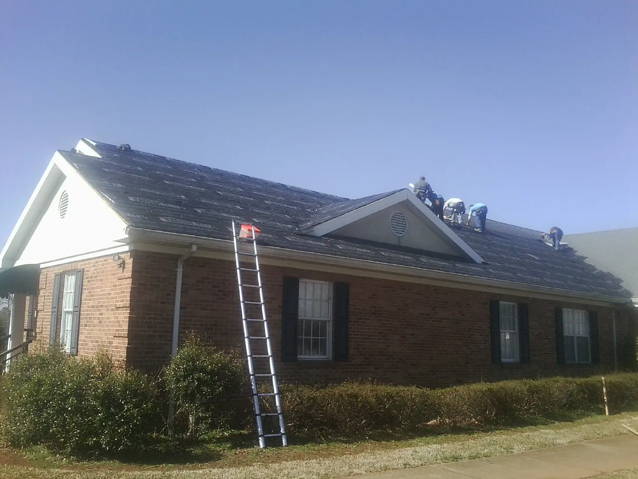 Crew tearing shingles off a brick ranch roof with a ladder set — Emergency Roof Repair work by our crew in Shoup
