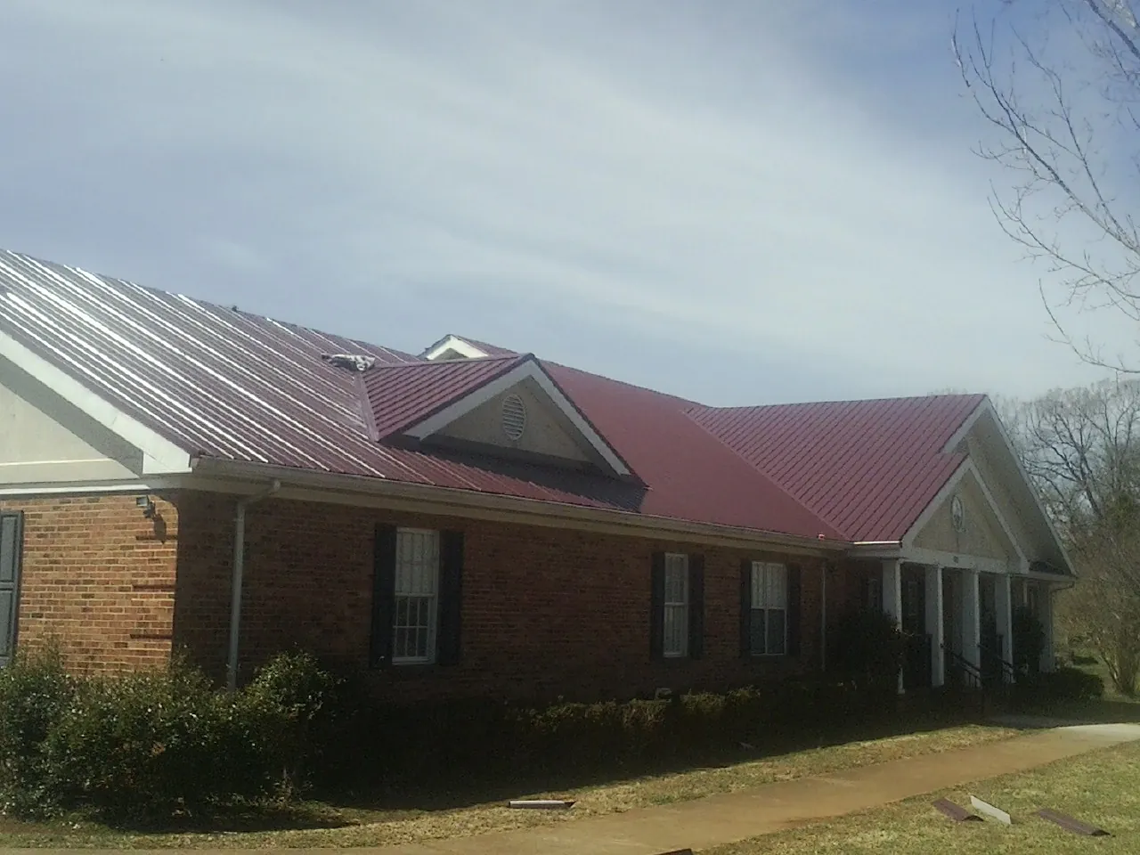 Red metal roof with gabled entries on a long brick building, from a Hail Damage Roof Repair job in Shoup