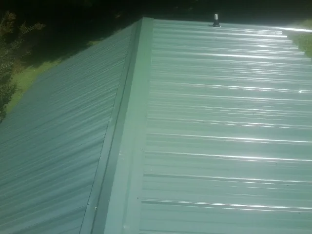 New green metal panels meeting at the ridge of a roof — Flat Roof Repair work by our crew in Shoup