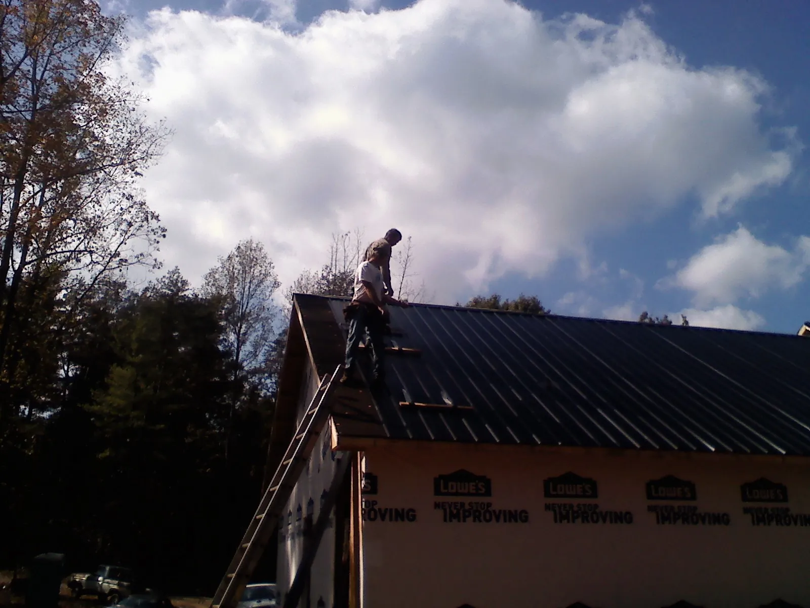 Roofer fastening dark metal panels high against a cloudy sky, from a Roof Inspection job in Shoup