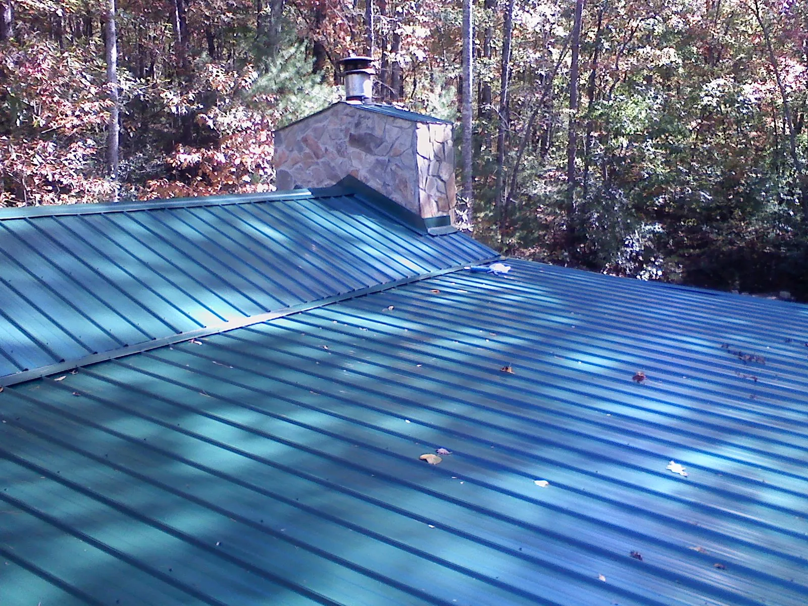 New green metal roof and stone chimney surrounded by autumn woods in Shoup