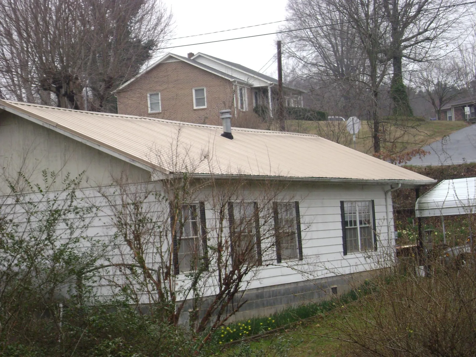 Tan metal roof on a white sided house set into a hillside — Commercial Roofing by Roofing Brothers in Shoup