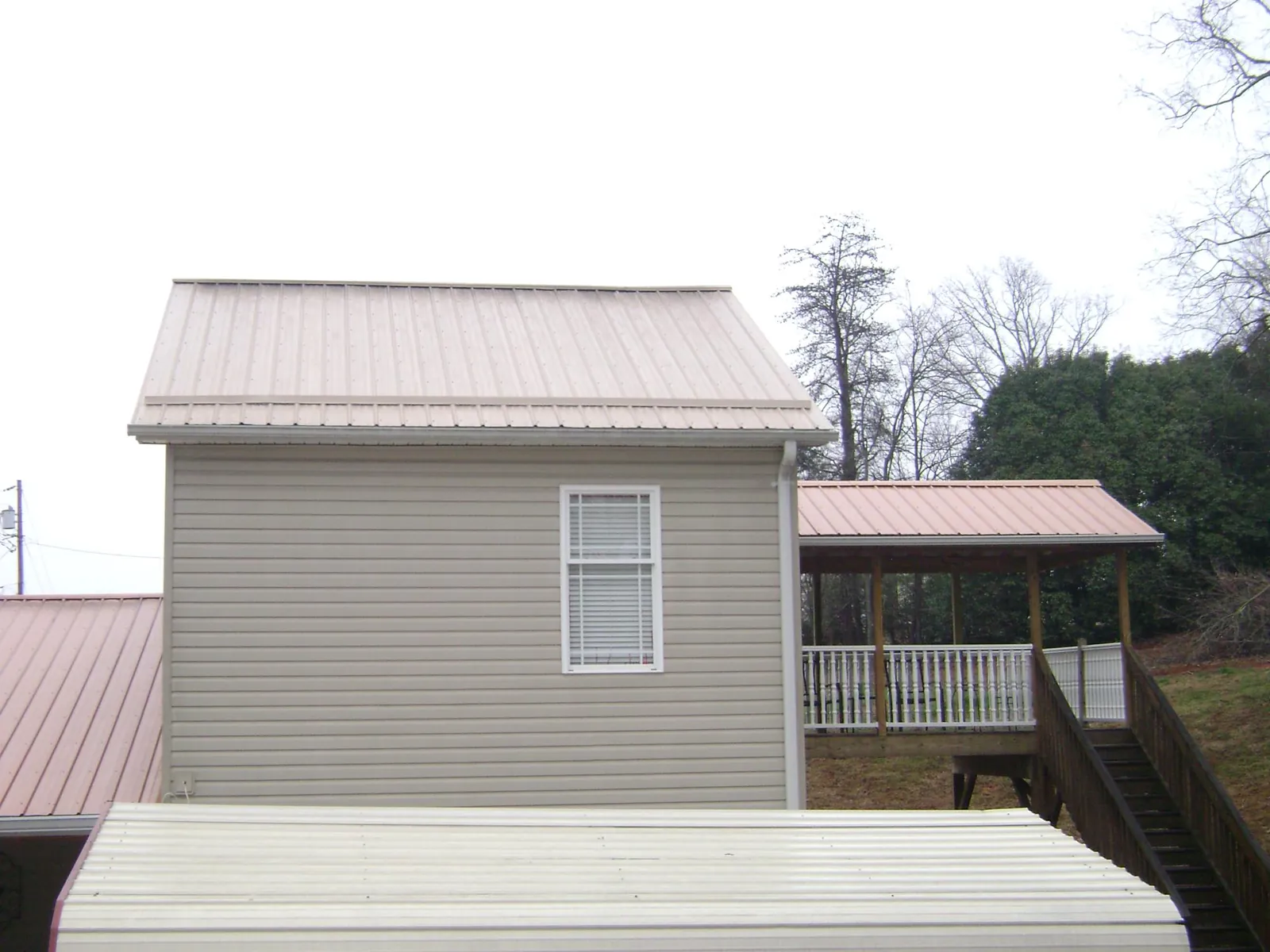 Tan metal roofs on a two story addition and attached porch, from a Roof Replacement job in Shoup